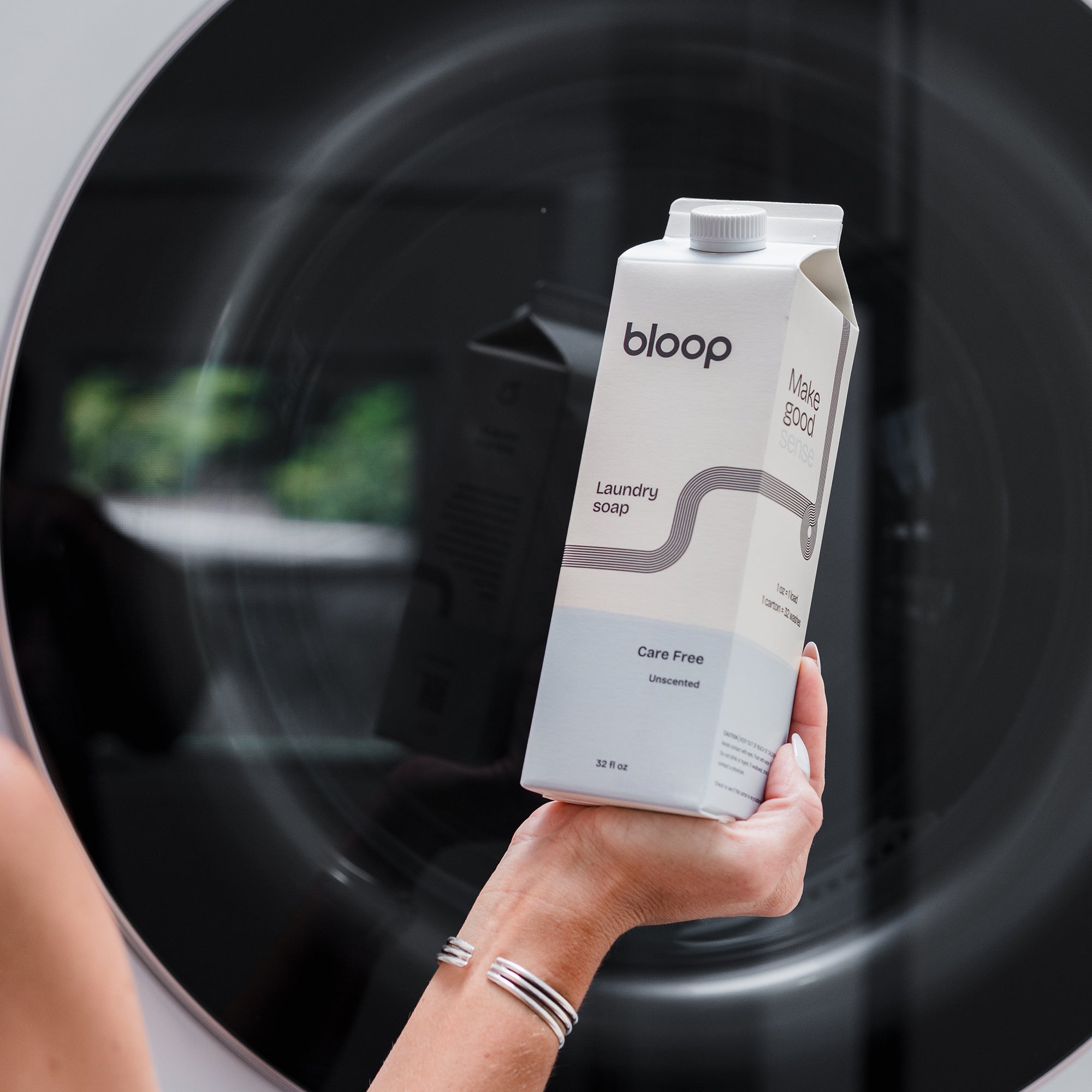 Front View of Care Free Natural Laundry Soap. 32 ounces. Plastic-free packaging. Laundry Soap being held up in front of washing machine.