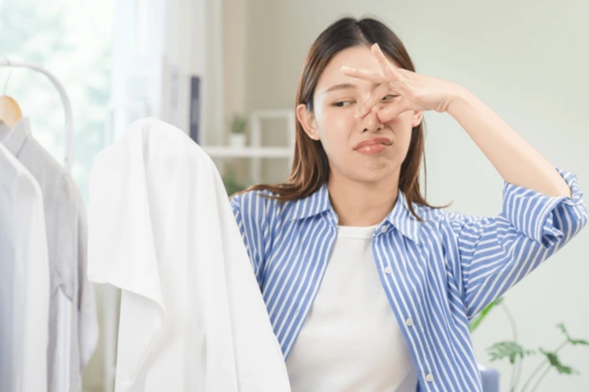 Woman smelling stinky laundry wondering how her clothes smell bad even after a wash cycle